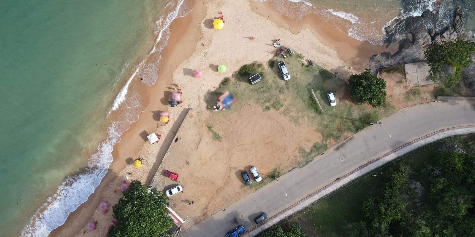 Vista aérea de uma praia do litoral capixaba, com carros estacionados no gramado e uma via que contorna a orla